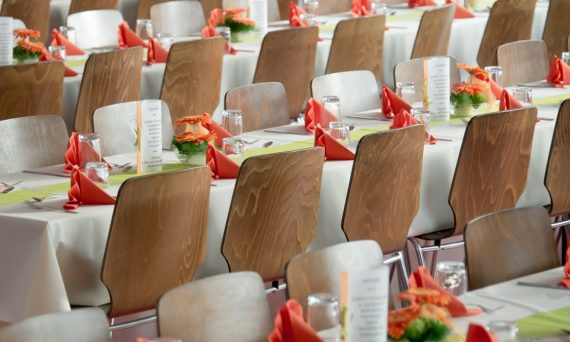 Beautifully arranged tables with wooden chairs for a formal event, adorned with orange flowers.