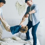 Mother father swinging child holding hands and feet then putting on bed at home