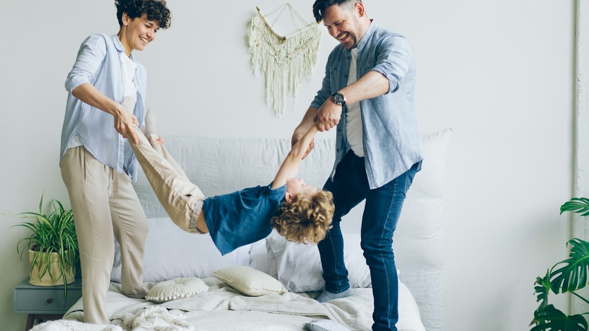 Mother father swinging child holding hands and feet then putting on bed at home